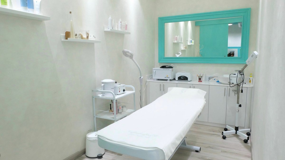 The white treatment room with a turquoise framed mirror and a made-up bed